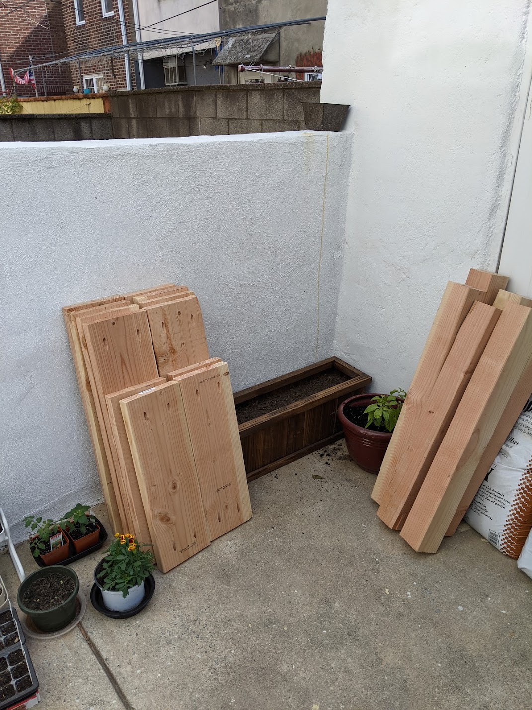 Back patio with lumber cut in different sizes, pre-drilled and waiting to be put together. A few potted plants are also on the ground.
