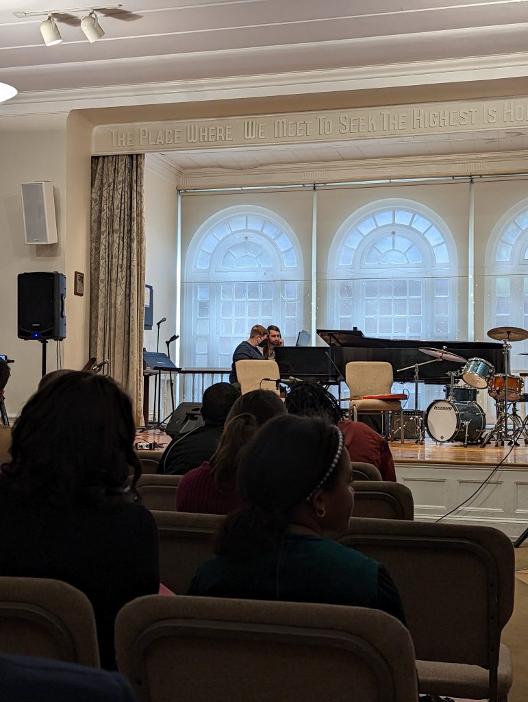 Mel and her music instructor on stage with assorted other instruments. Mel is playing the piano.