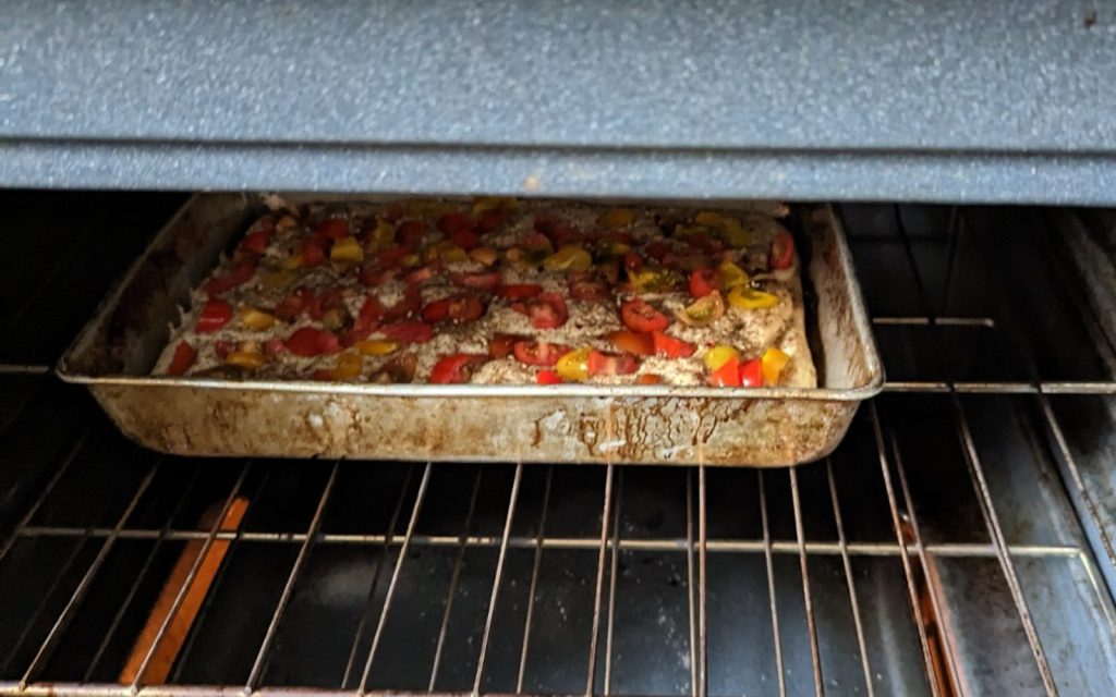 A baking tray in the oven with bread topped with red, orange, and yellow cherry tomatoes.