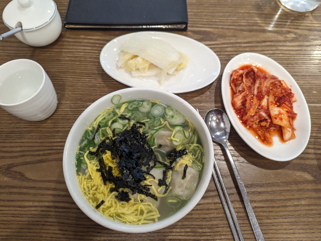 Three dishes on a table: white kimchi, red kimchi, and dumpling soup.