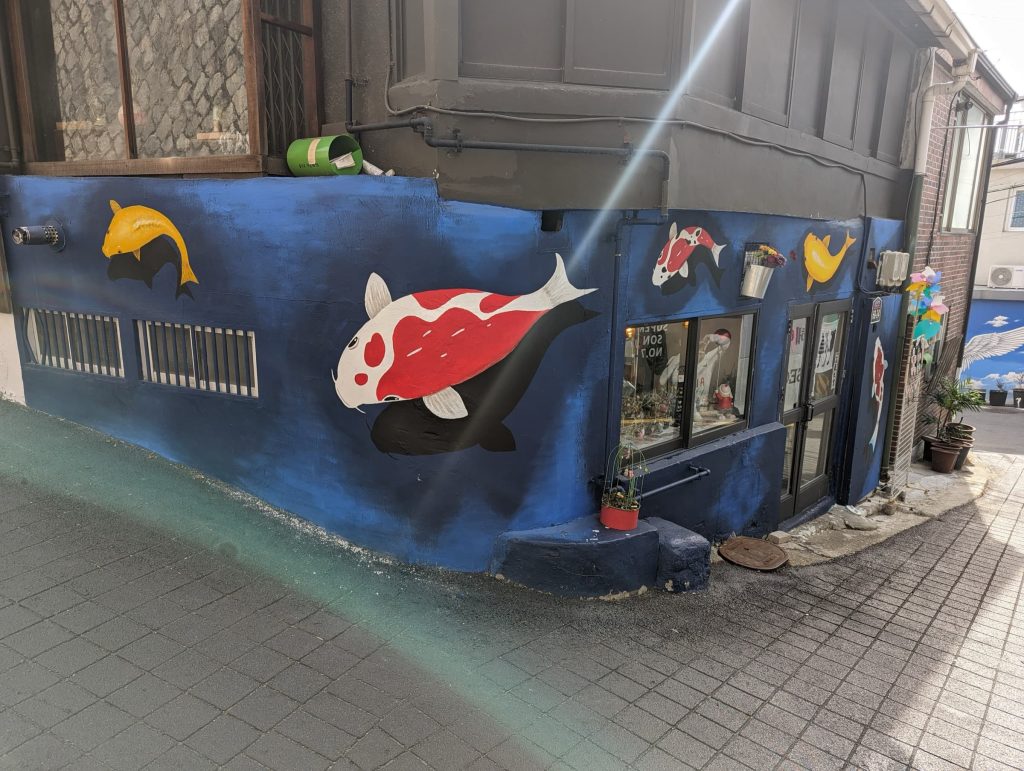 The outside of a building, painted dark blues with vibrant Koi fish. The mural wraps around the front and side.