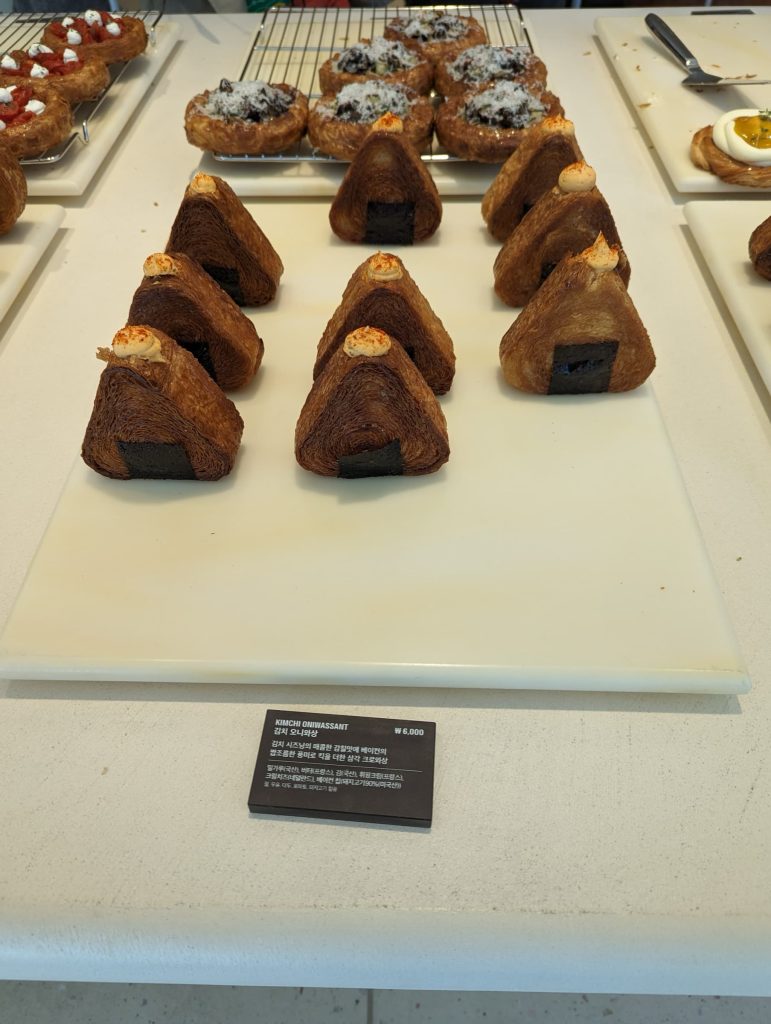 A display of triangle-shaped pastry swirled with layers like a croissant, topped with a cheese cream. Other pastries are on display in the background.