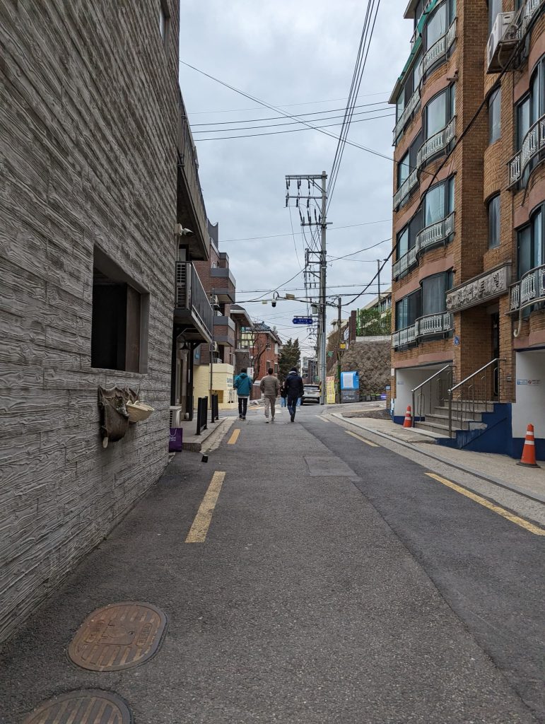 A small street in Seoul, with 3 guys walking side by side.
