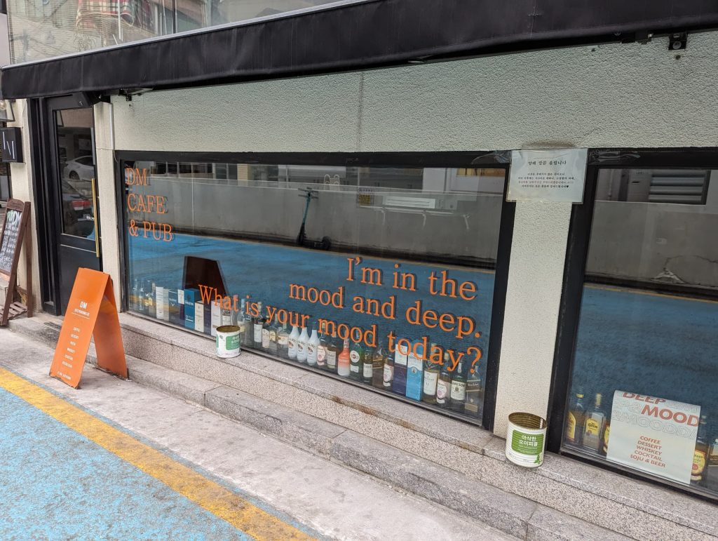 A bar window spanning the wall, with alcohol bottles lining the bottom. There's text on the window: "I'm in the mood and deep. What is your mood today?"