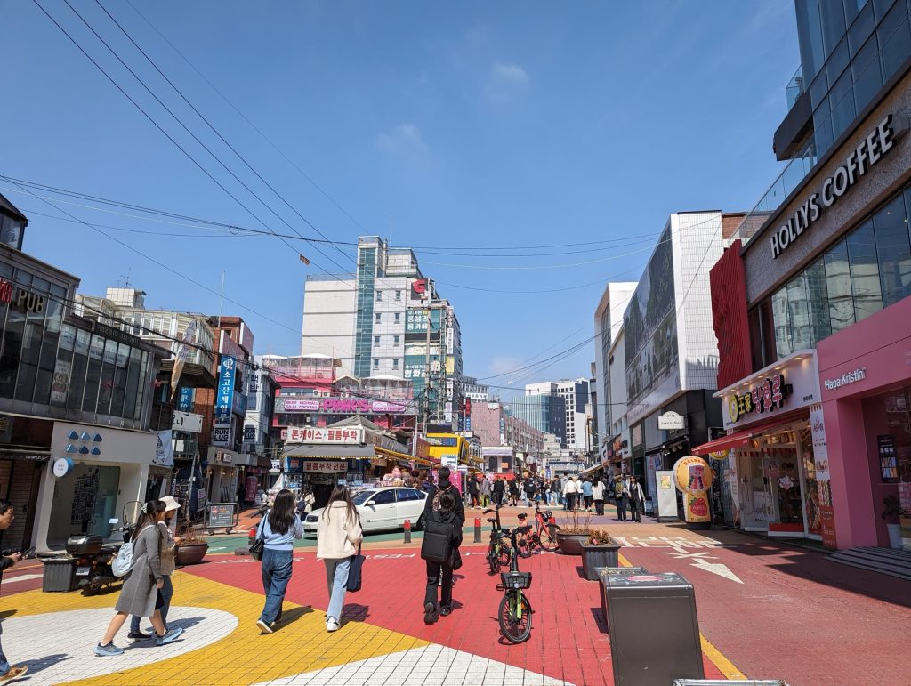A brightly painted street with a large pedestrian walkway down the center. Shops and restaurants line the street.