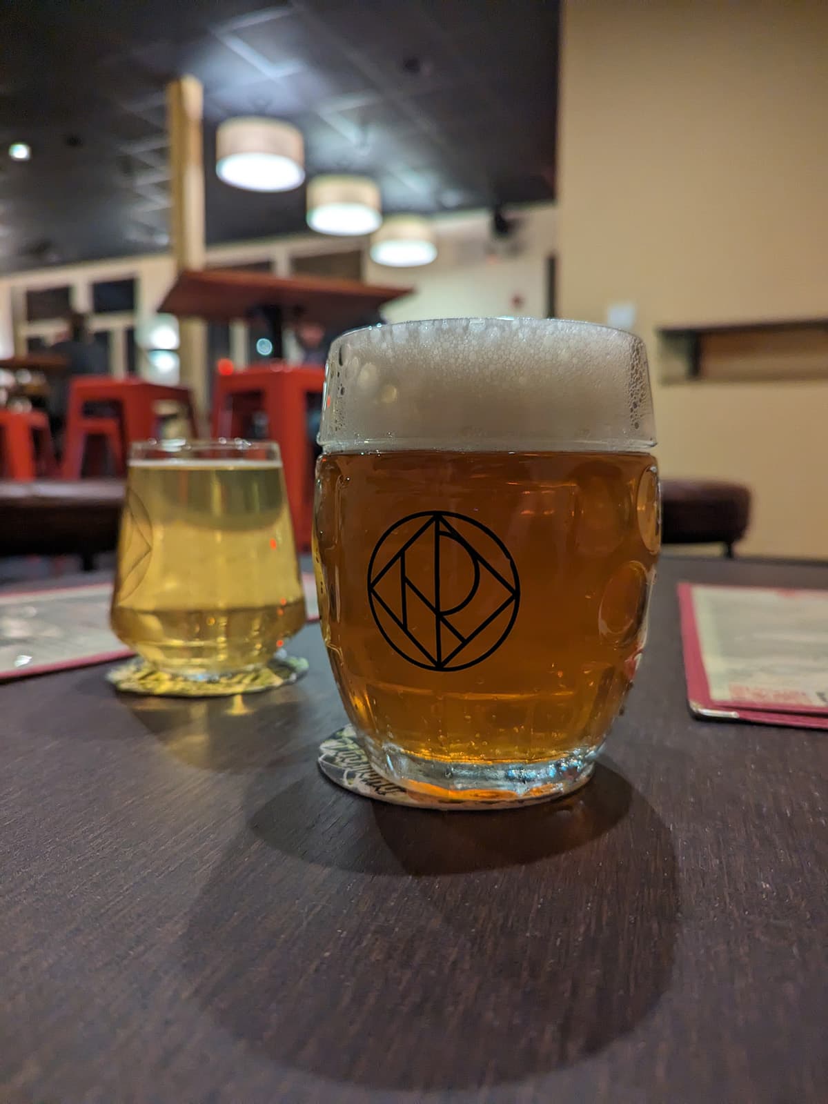A mug of beer centered, with a glass of cider behind it.
