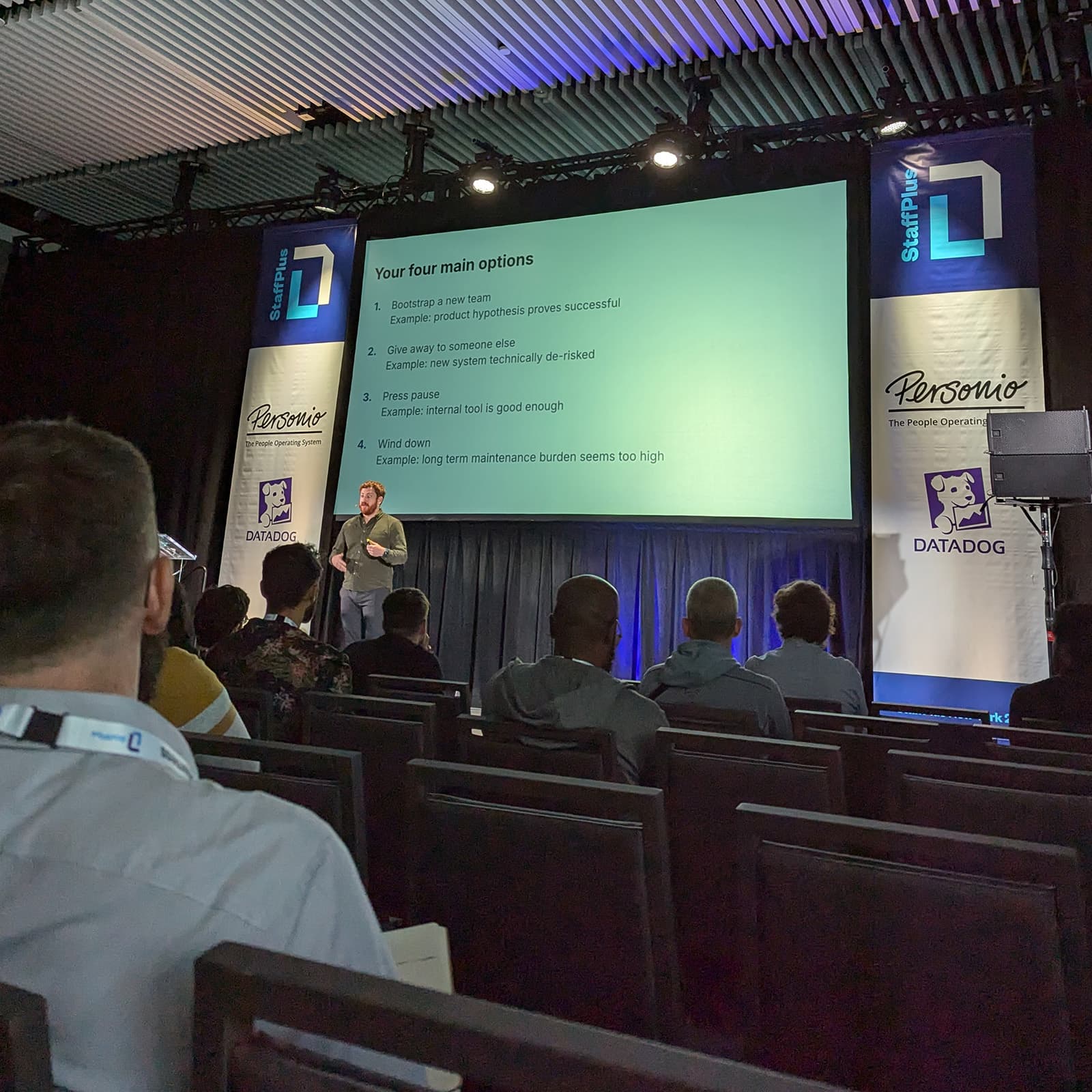 View from the audience of a stage with a speaker and slides.