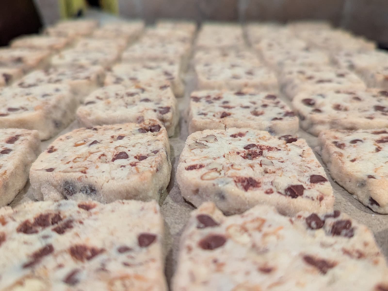 Close-up photo of many rows of shortbread cookies, with chocolate chips, nuts, and pretzel pieces.