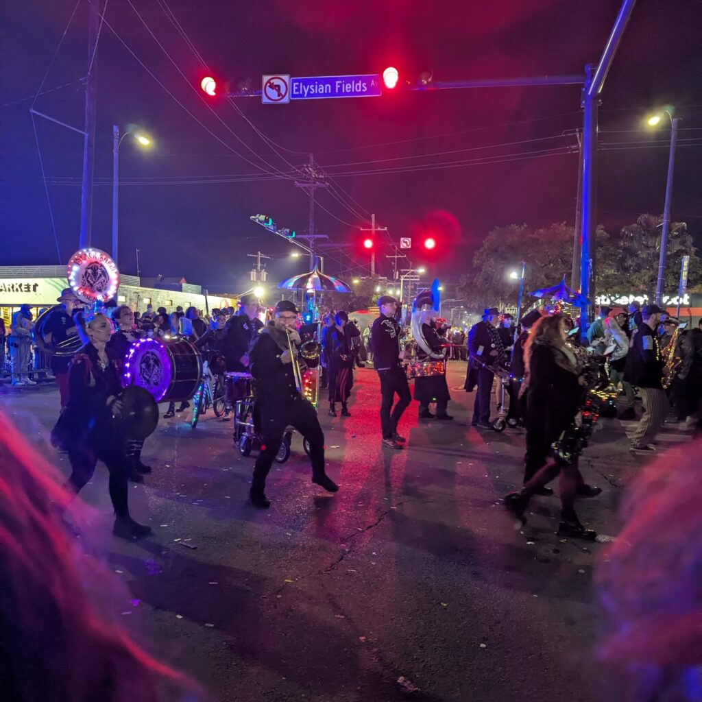 Nighttime, street view of a parade of musicians in old-style circus costumes.