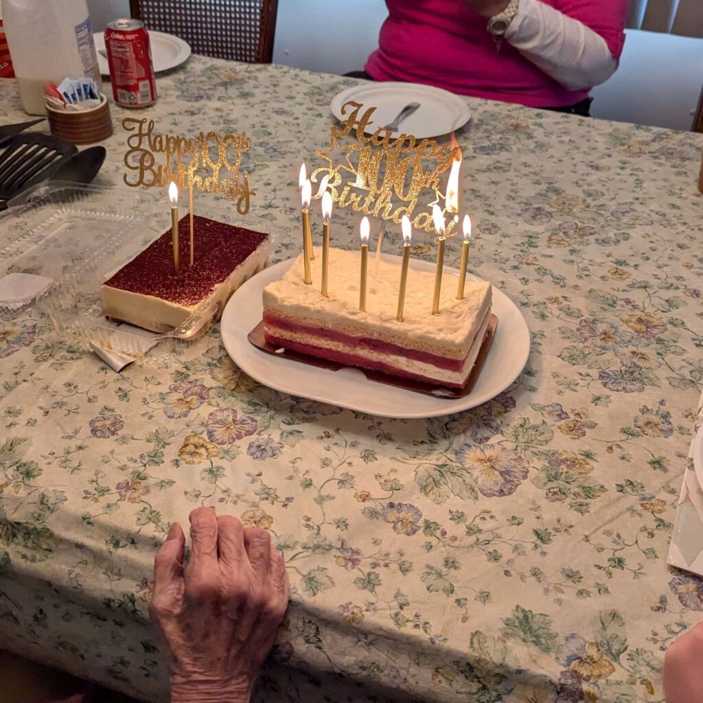Two cakes with Happy Birthday signs and lit candles, one says "Happy 100th Birthday" and has just caught fire.