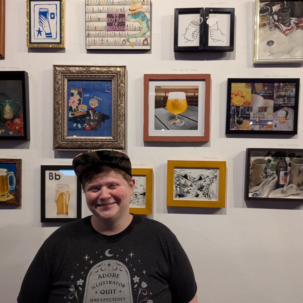 Mel in front of a wall of artwork, her piece is a digital painting in color of a beer glass on a wooden outdoor table.